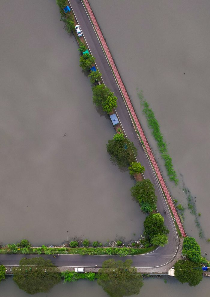 Crafting Captivating Headlines: Your awesome post title goes here Top-down aerial view of a road partially submerged during a flood, surrounded by water and greenery.